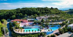 Veduta aerea di un resort con piscine e vegetazione collinare attorno.