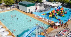 Vista aerea di una piscina con scivoli e area giochi colorata, circondata da let