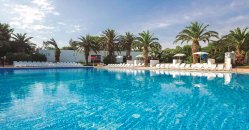 Piscina con lettini bianchi e palme intorno sotto un cielo parzialmente nuvoloso