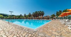 Piscina con sdraio e ombrelloni arancioni intorno, cielo blu e alberi sullo sfon