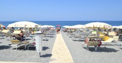 Spiaggia con ombrelloni bianchi e lettini su sabbia chiara. Sfondo di mare blu.