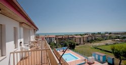 Vista dal balcone di un edificio con piscina e mare in lontananza.